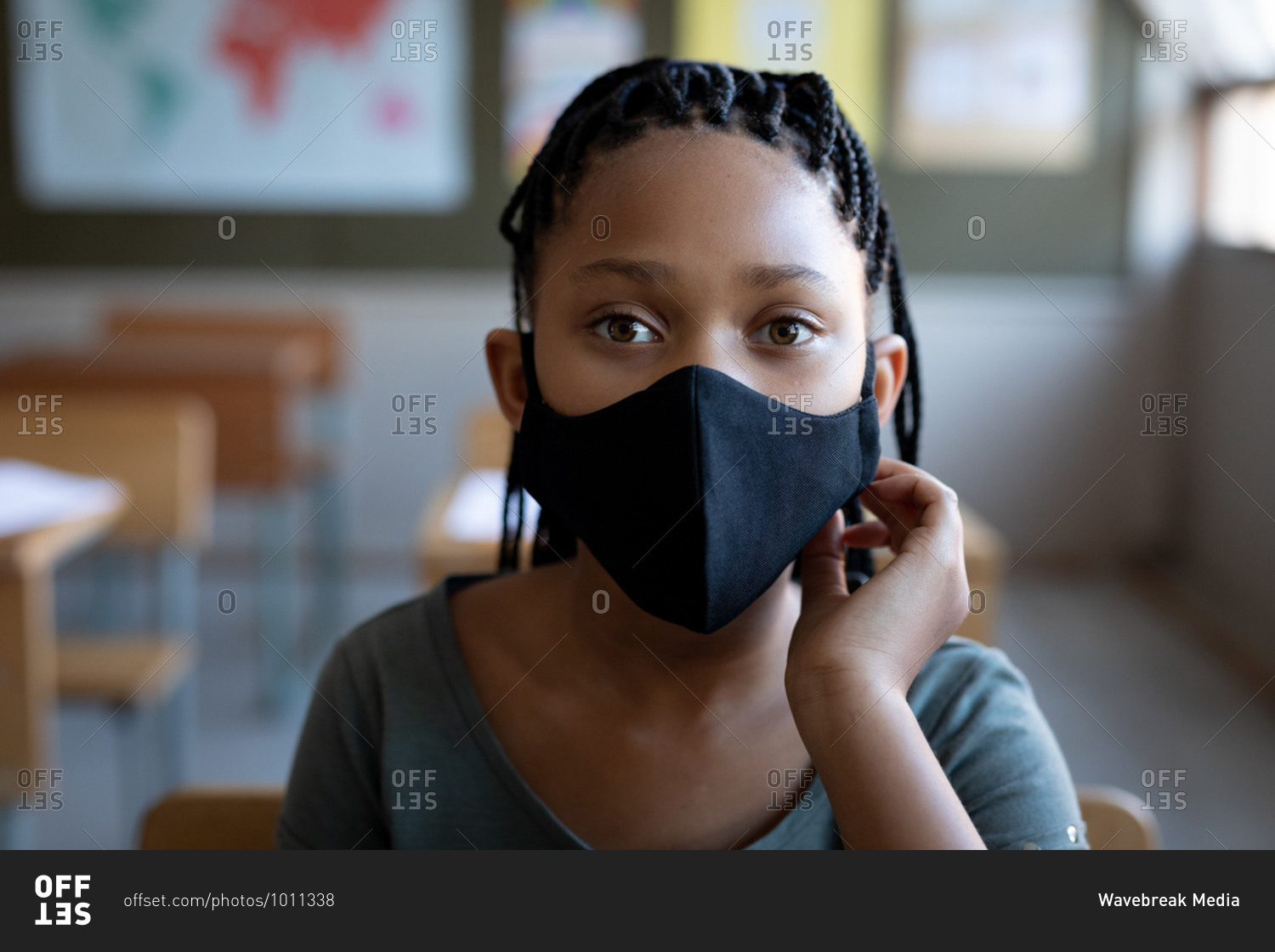 Portrait of a mixed race girl wearing a face mask, sitting on his desk in class at school. Primary education social distancing health safety during Covid19 Coronavirus pandemic.