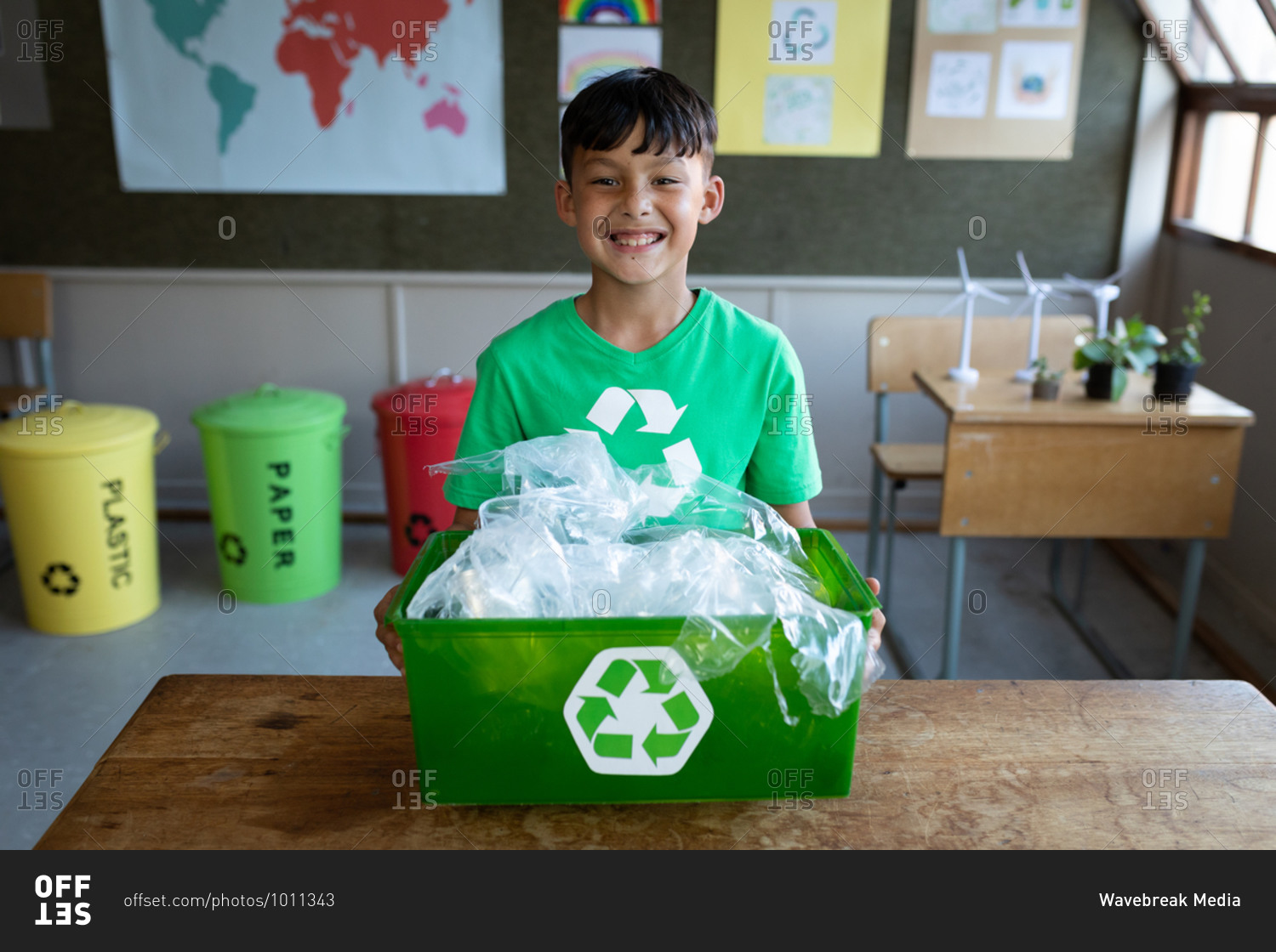 Portrait of a mixed race boy holding a recycle container in class at school. Primary education social distancing health safety during Covid19 Coronavirus pandemic.