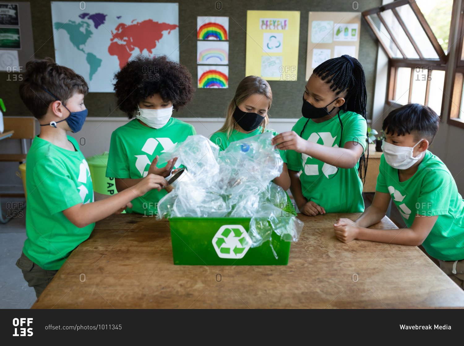 Group of multi ethnic kids wearing face masks holding plastic items in class at school. Primary education social distancing health safety during Covid19 Coronavirus pandemic.