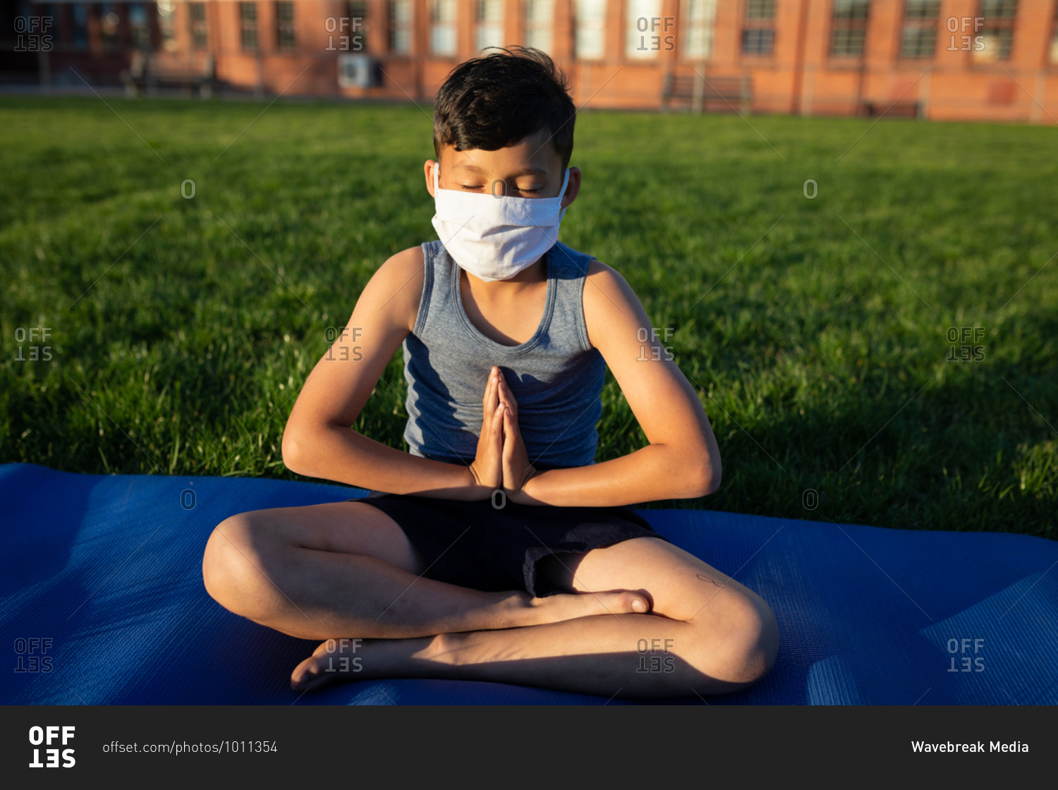 Mixed race boy wearing face mask performing yoga in the school garden. Primary education social distancing health safety during Covid19 Coronavirus pandemic.