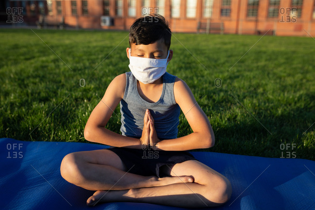 Mixed race boy wearing face mask performing yoga in the school garden. Primary education social distancing health safety during Covid19 Coronavirus pandemic.