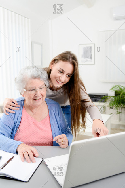 Young woman helping old senior woman doing paperwork and administrative procedures with laptop computer at home