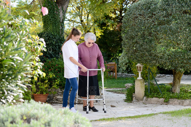 Elderly senior woman with a nurse walking outdoor in nursing home hospital garden
