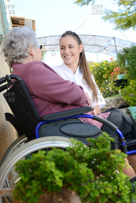 Elderly senior woman on wheelchair with a nurse outdoor in nursing home hospital garden.