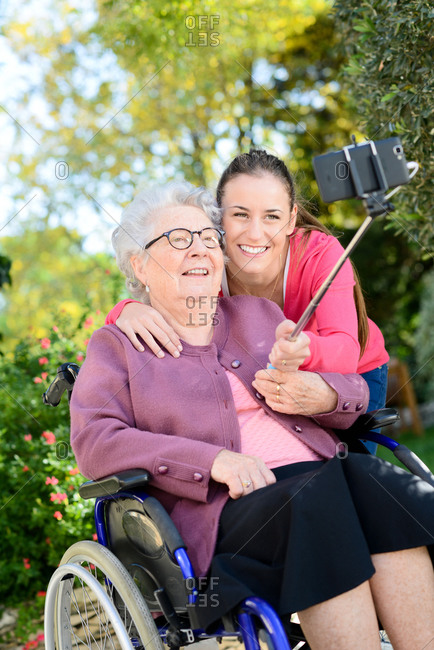 Cheerful young woman making a selfie with a elderly senior woman in a retirement house garden.