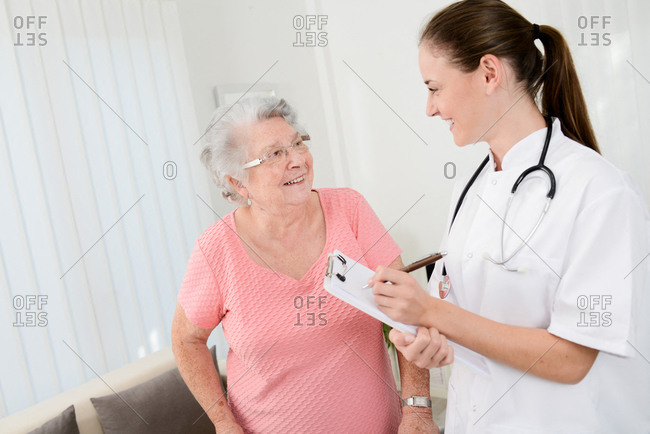 Young doctor checking rehab medical progress to elderly woman at home.