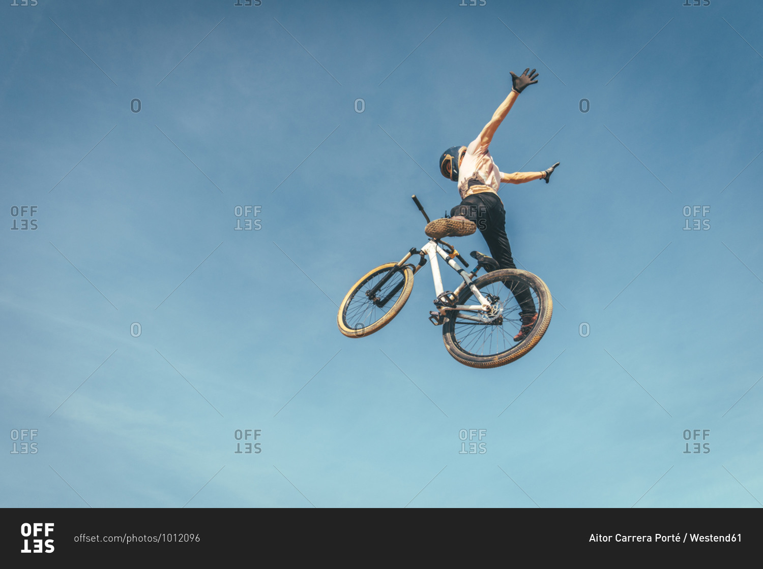 Carefree man performing stunt with bicycle against blue sky during sunset