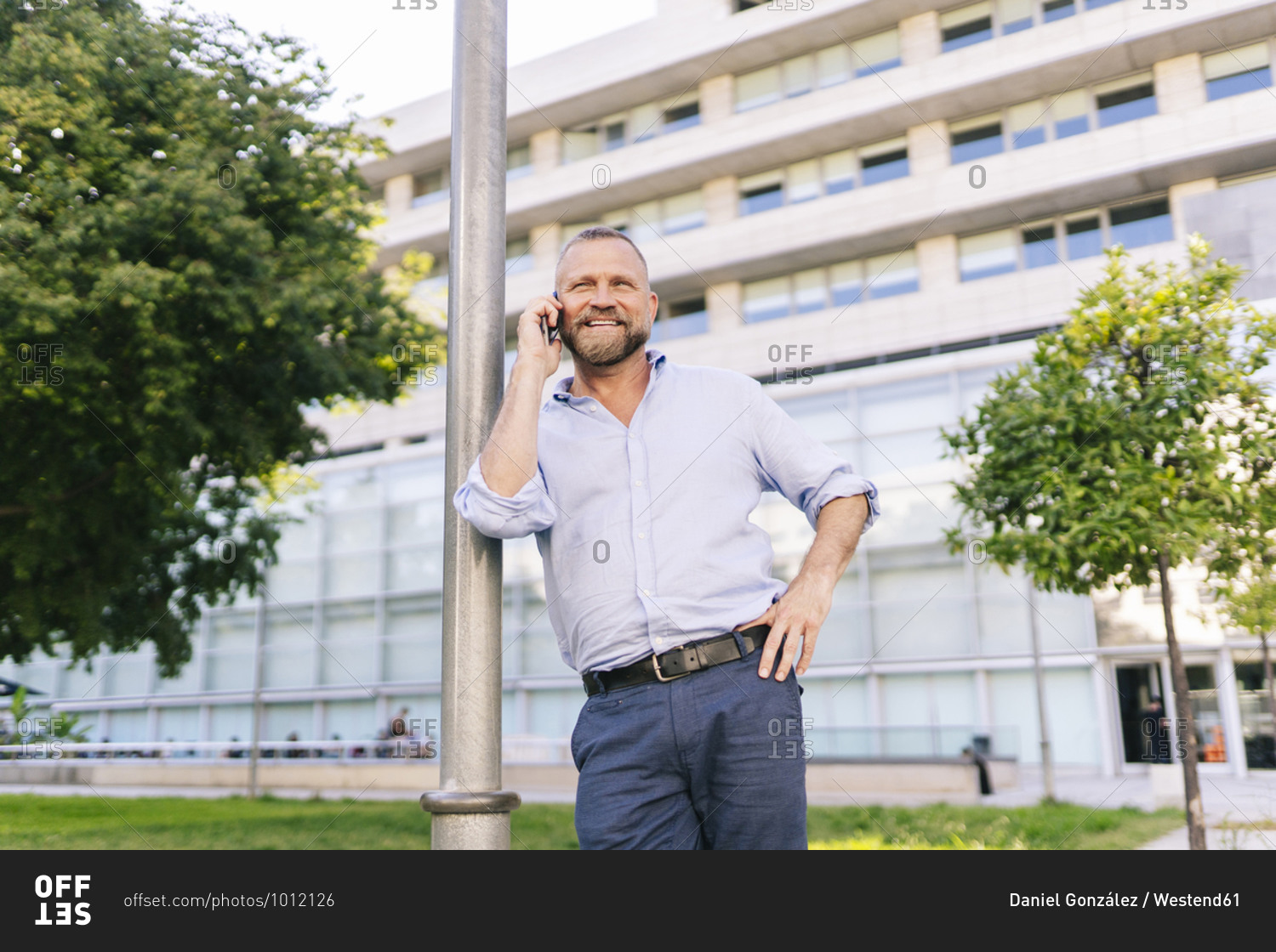 Smiling businessman talking on mobile phone while leaning on pole at office park