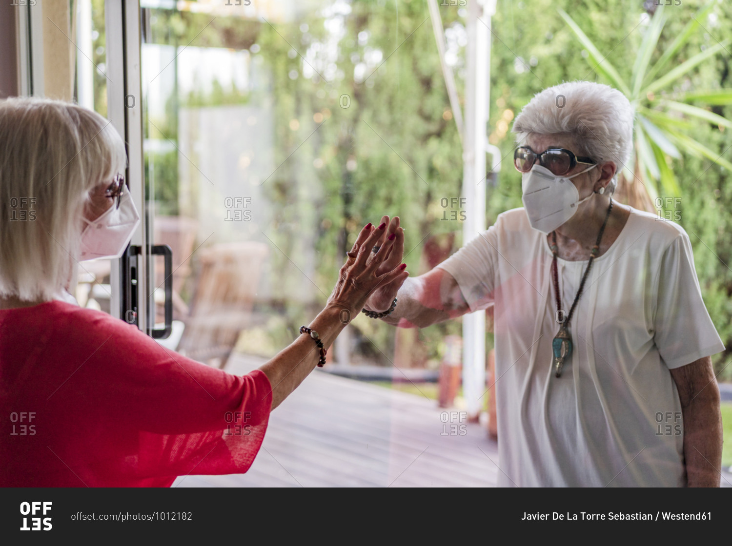 Senior female friends wearing masks looking at each other through window