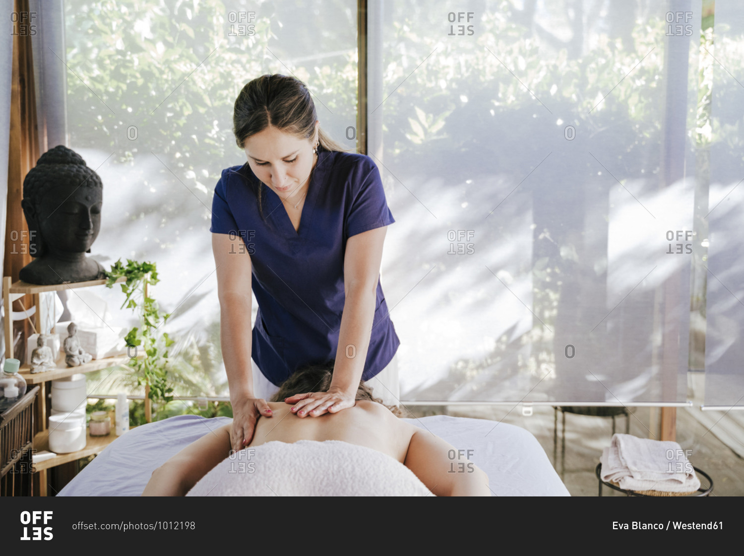 Mid adult woman giving back massage to female customer lying on table in spa