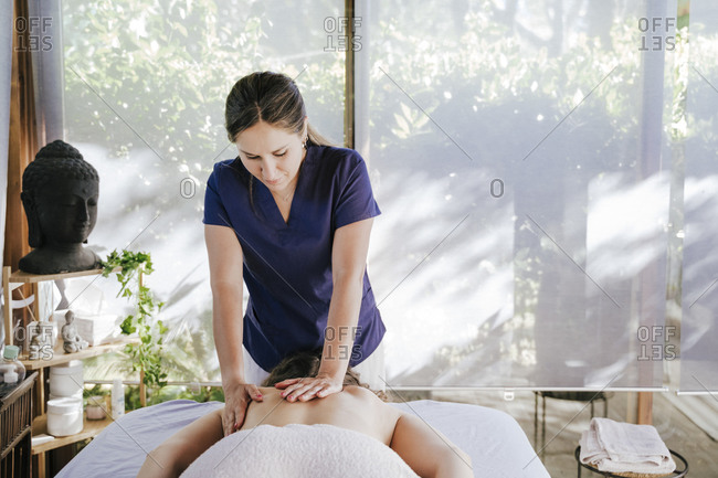 Mid adult woman giving back massage to female customer lying on table in spa