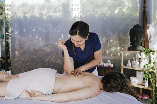 Female therapist massaging shirtless woman\'s back relaxing on table in spa