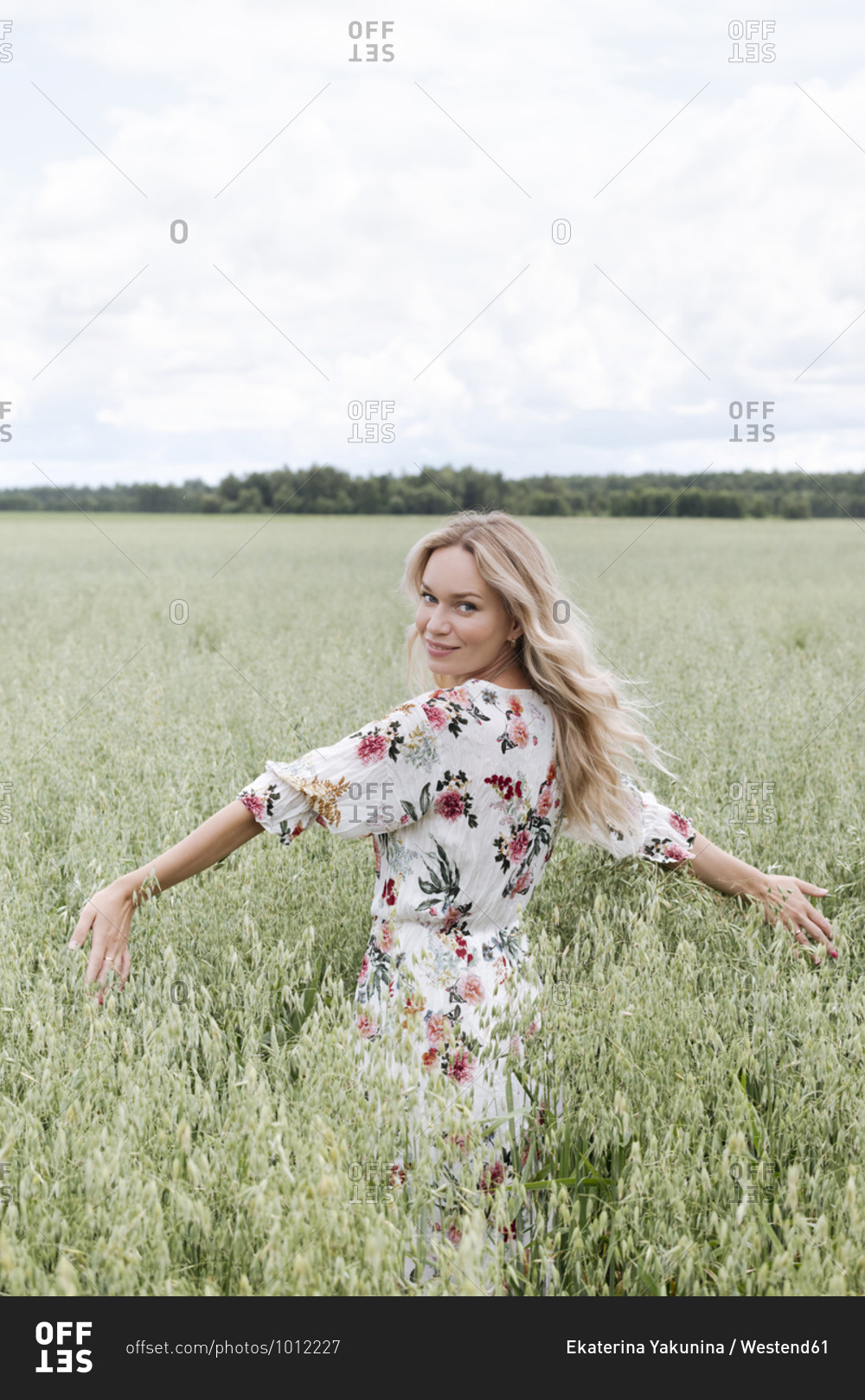 Beautiful woman with blond hair standing amidst oats field against cloudy sky