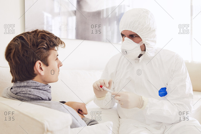 Doctor wearing protective suit explaining about medical test to patient at home