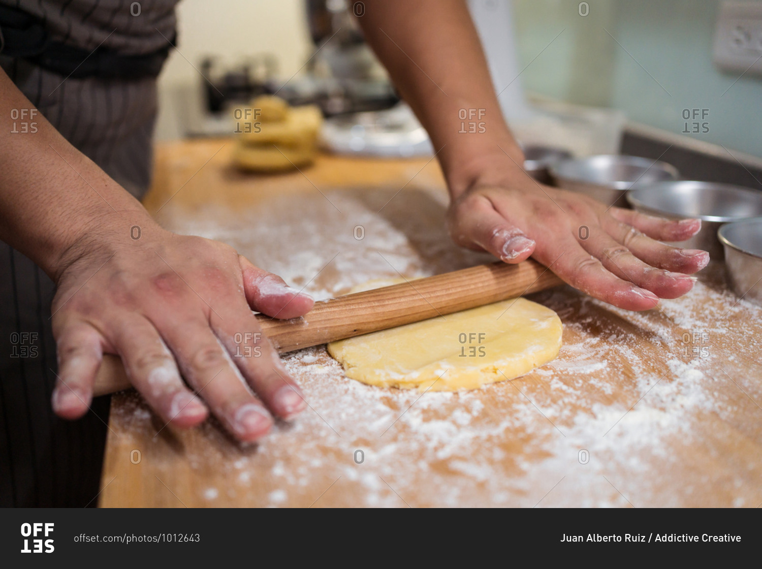 Cropped unrecognizable person in apron rolling dough with rolling pin working at home