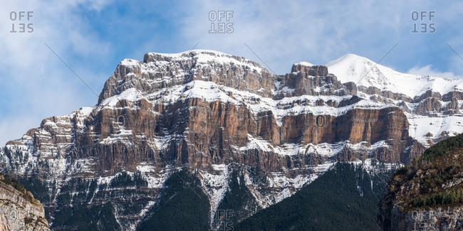 Spectacular landscape of mountain with snowy peak on slope under blue cloudy sky in sunny autumn day
