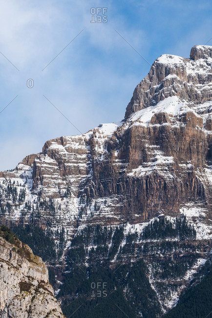 Spectacular landscape of mountain with snowy peak on slope under blue cloudy sky in sunny autumn day