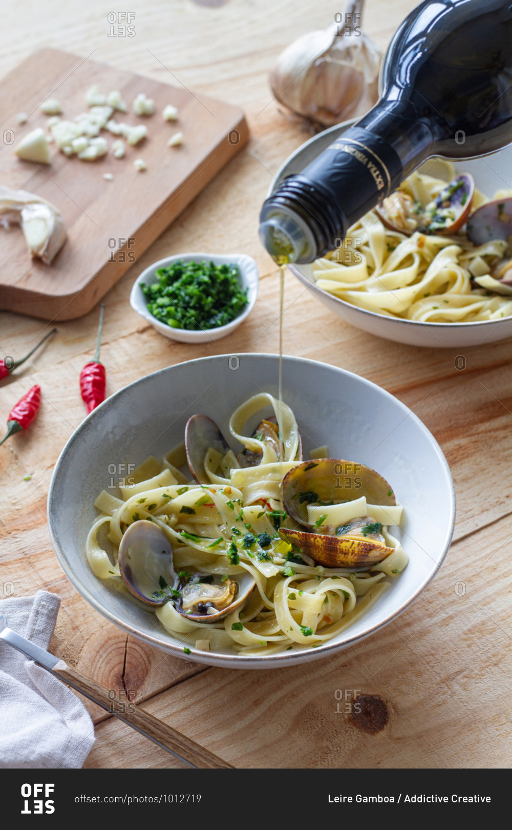Unrecognizable cook pouring olive oil in bowl with spaghetti and clams placed on wooden table in restaurant