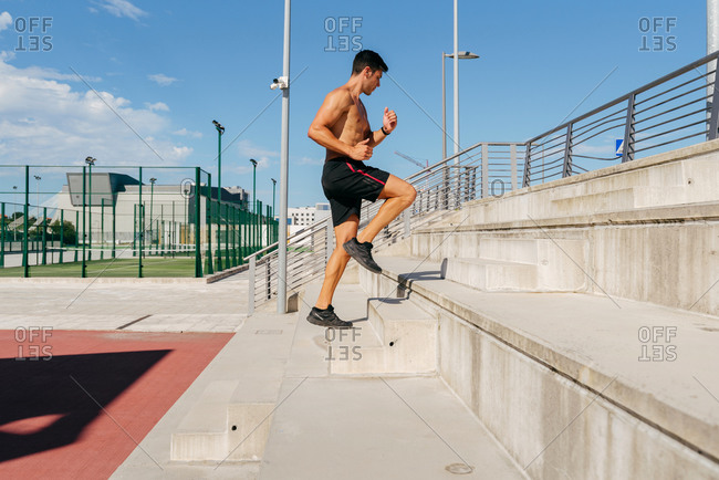 Side view of confident male athlete running up stone steps during intense workout on sunny day in summer