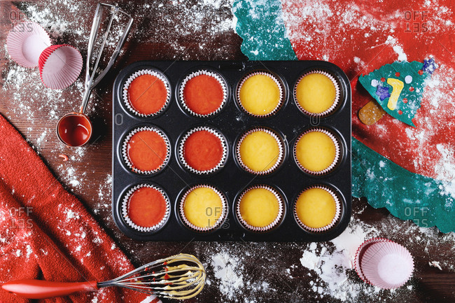 Top view of metal baking dish with paper cupcake cups filled with colorful dough during pastry preparation for Christmas holiday