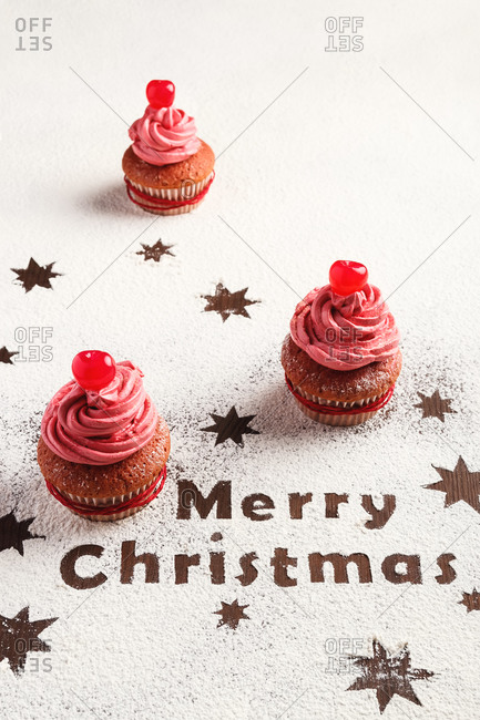 From above of delicious sweet cupcakes with pink frosting arranged on table sprinkled with sugar powder and decorated with stars and Merry Christmas text