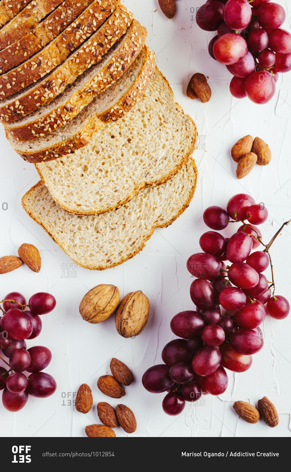 Top view composition with sliced bread and red and green grapes arranged on white table with walnuts and almonds