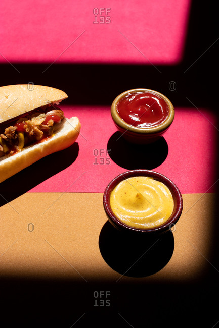 From above frankfurt hot dog with mustard and ketchup served on small bowls on colorful background