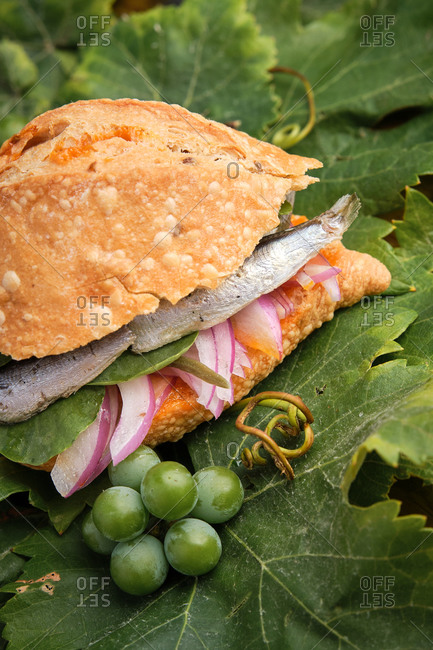 Vertical photo of the traditional harvest sandwich with sardines, meat and different vegetables on top of a grapevine leaf. Gastronomy of Canary Islands