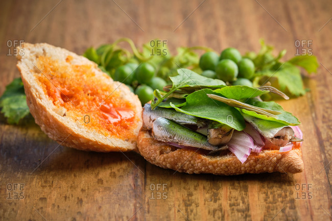 Half opened traditional harvest sandwich with sardines, meat and different vegetables on a wooden surface with some grapevine leaf on the side. Gastronomy of Canary Islands