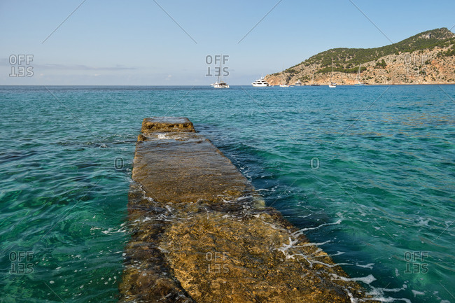 Amazing scenery of turquoise water of sea with stone quay on background of blue cloudless sky