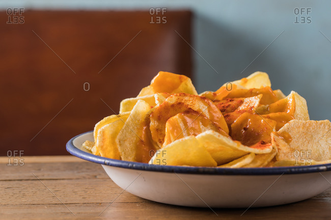 High angle of pile of crispy potato chips in bowl placed on wooden table at home