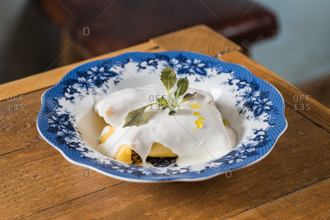 Closeup of plate of palatable ravioli garnished with bechamel sauce and sprig of fresh herb