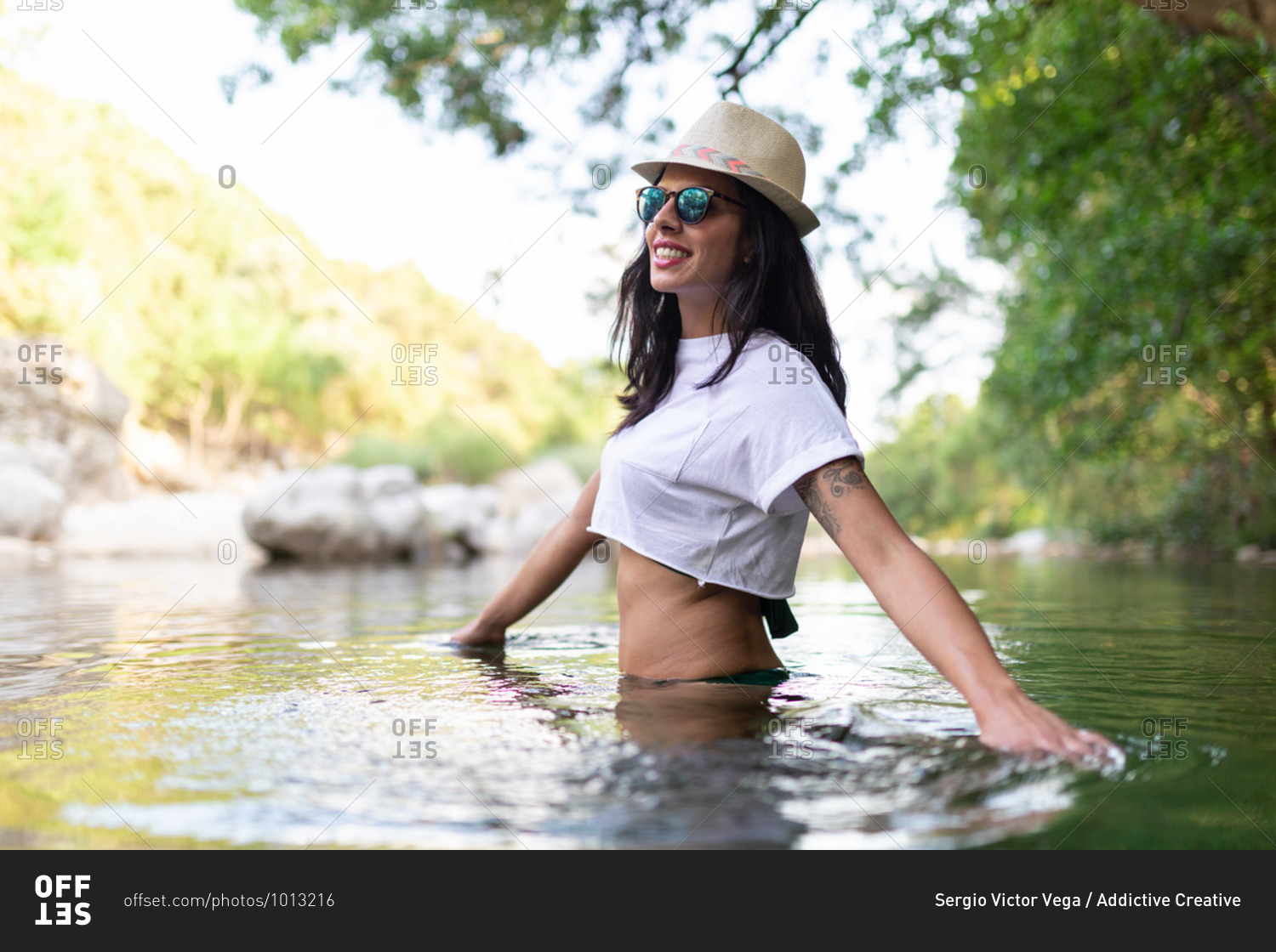 Carefree female traveler standing in calm water of pond and enjoying summer vacation in forest