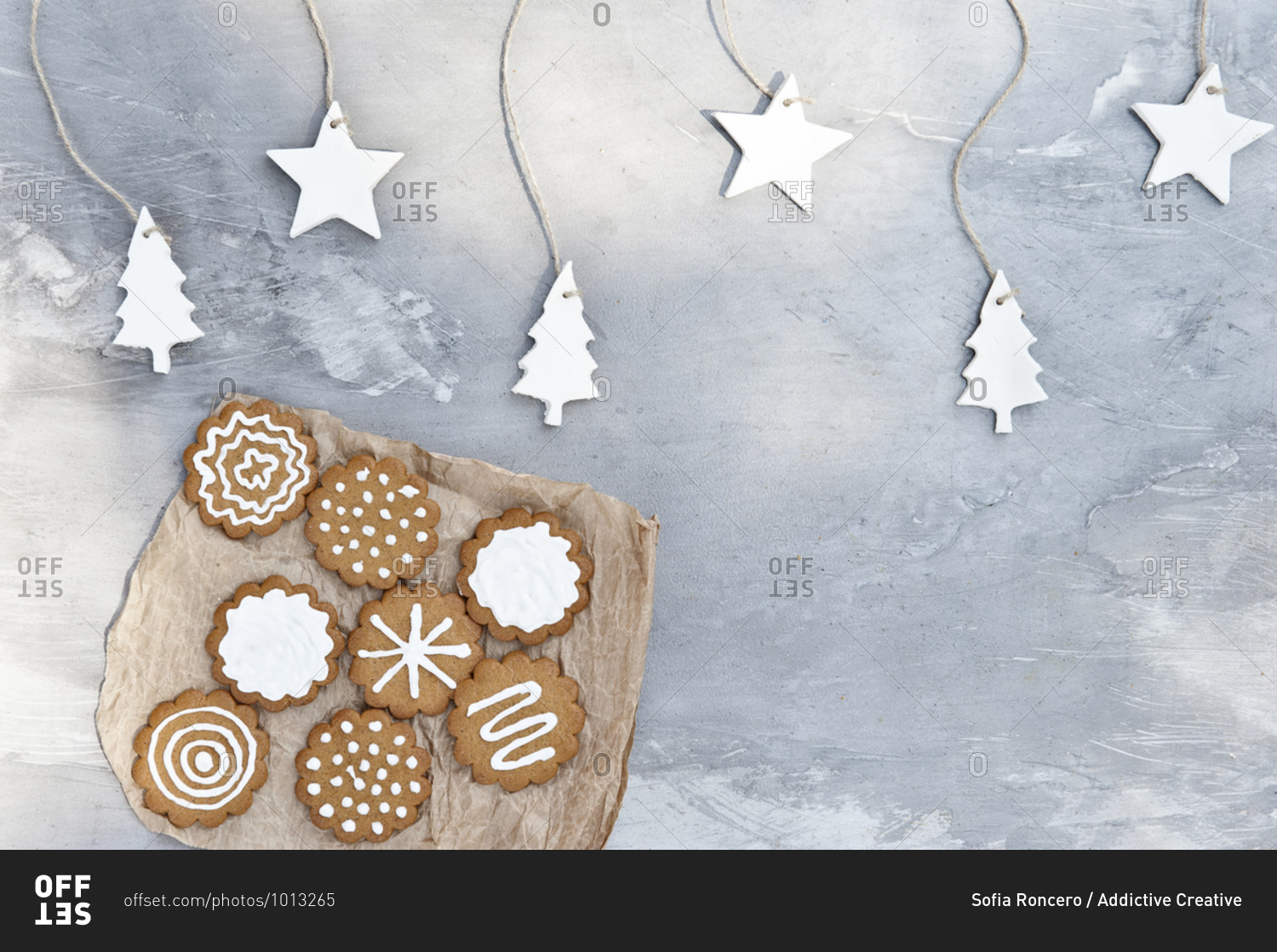 Plate with assorted gingerbread cookies with white icing placed near gray wall decorated with craft star and tree shaped paper items