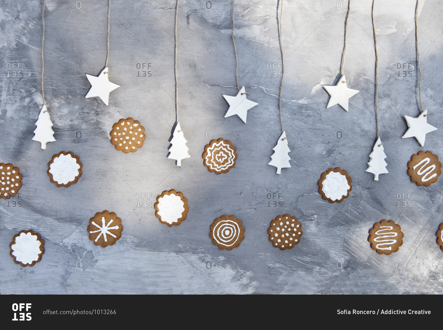 Plate with assorted gingerbread cookies with white icing placed near gray wall decorated with craft star and tree shaped paper items
