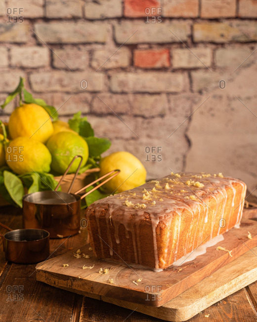 Delectable homemade whole lemon and poppy seeds cake garnished with sugar glaze and lemon zest served on wooden board on table with ingredients
