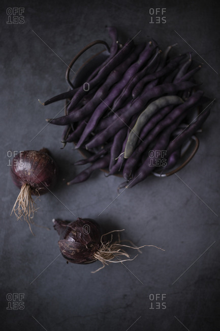 Fresh purple pea pods and red onions on a dark gray concrete surface