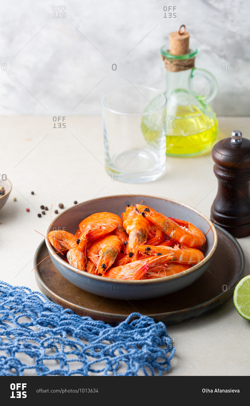 Shrimps in bowl on light table by oil and pepper