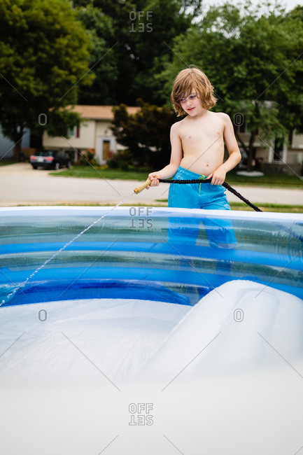 Boy filling up inflatable swimming pool with garden hose
