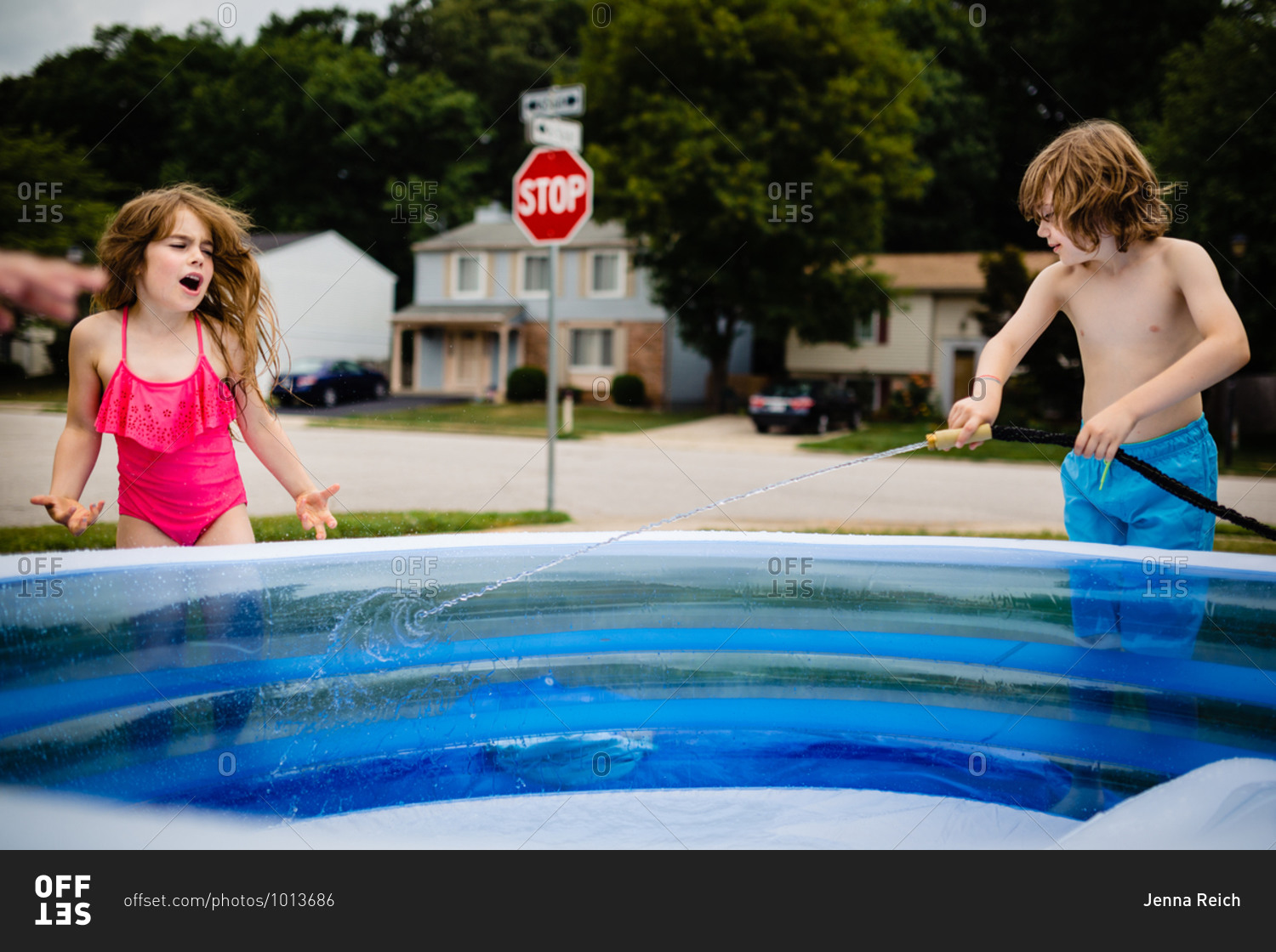 Boy spraying sister while filling up inflatable swimming pool with garden hose