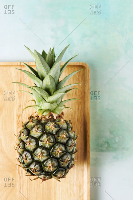 Overhead shot of small pineapple on a wood tray over a blue/green tabletop.