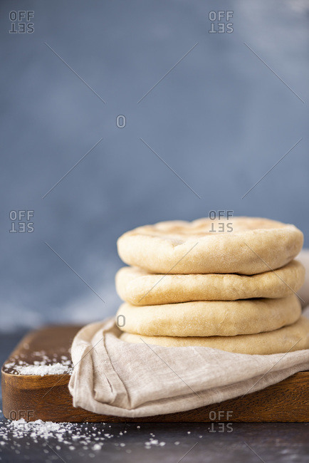 A stack of Turkish flatbread called bazlama on a wooden board, some sea salt on the side accompanies.