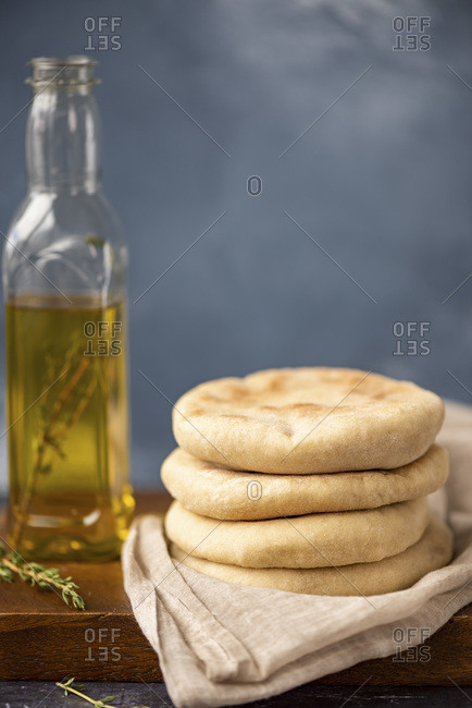 A stack of Turkish flatbread called bazlama on a wooden board, a bottle of olive oil and fresh thyme accompany.