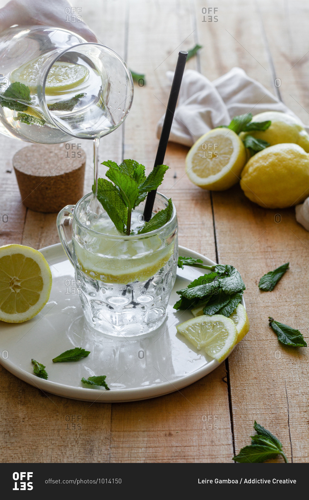 Cold refreshing drink with soda water and lemon garnished with fresh mint leaves served on glass cup with straw on wooden table