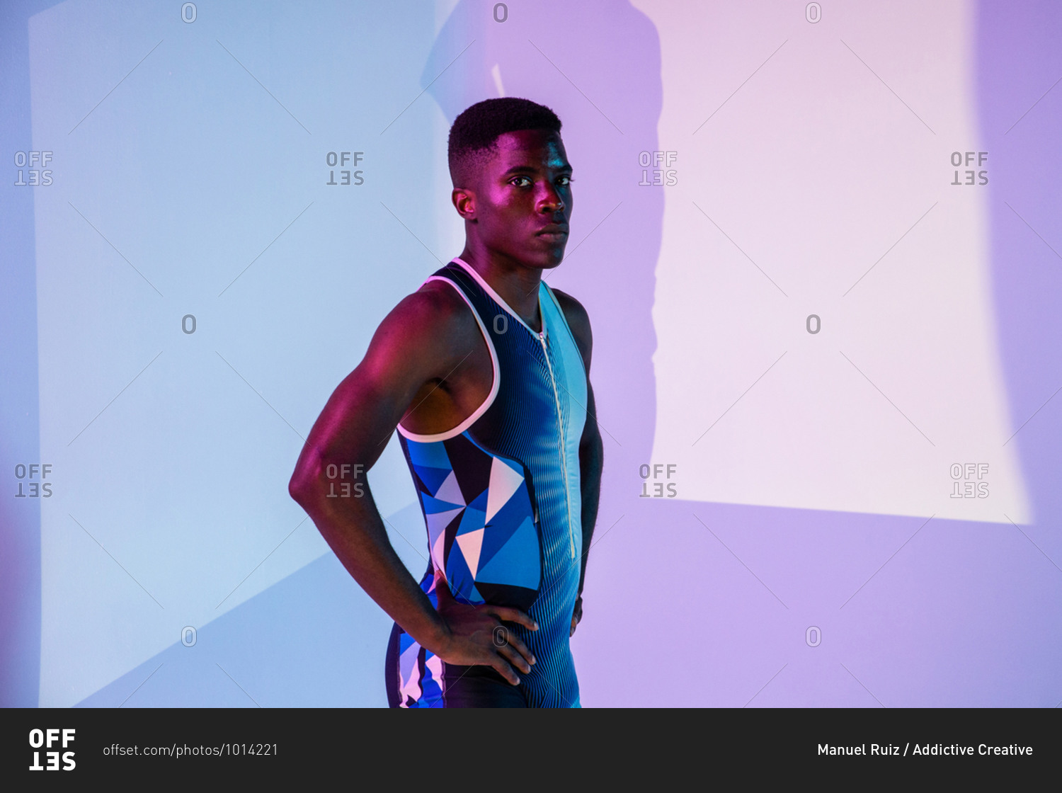 Full body side view of energetic young African American male sprinter standing against purple neon background looking at camera