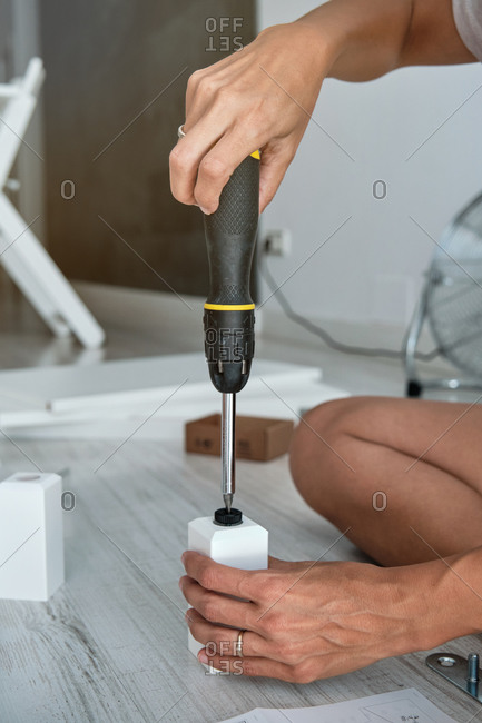 Side view of crop unrecognizable person using screwdriver and fixing details while assembling furniture at home