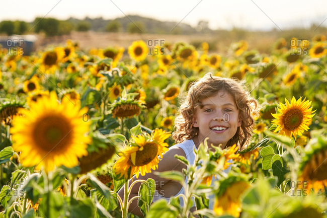 Smiling teenager standing in blossoming sunflower meadow in countryside and looking at camera while enjoying summer