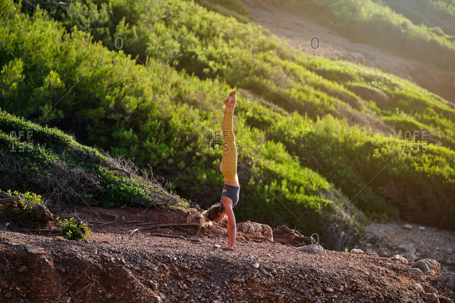 Woman in sportswear doing the handstand yoga position with her feet up and her hands resting on a wooden board in the middle of the forest