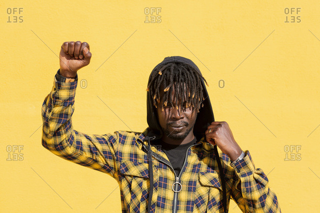 Attractive young black man with raised fist and hood on an intense yellow background, concept of human rights struggle and lifestyle