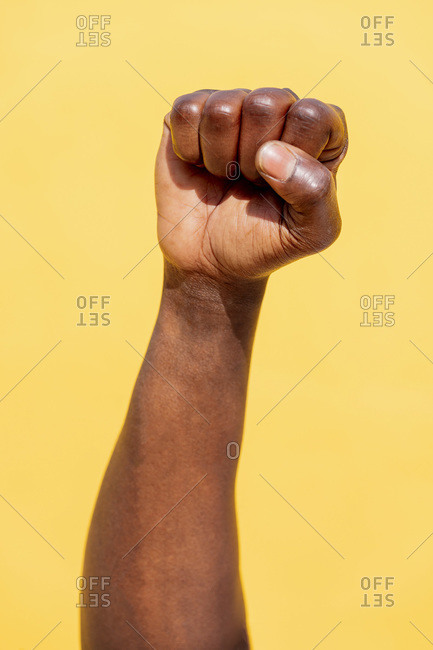 Vertical photo of a raised fist of a black man on an intense yellow background, concept of human rights struggle and lifestyle